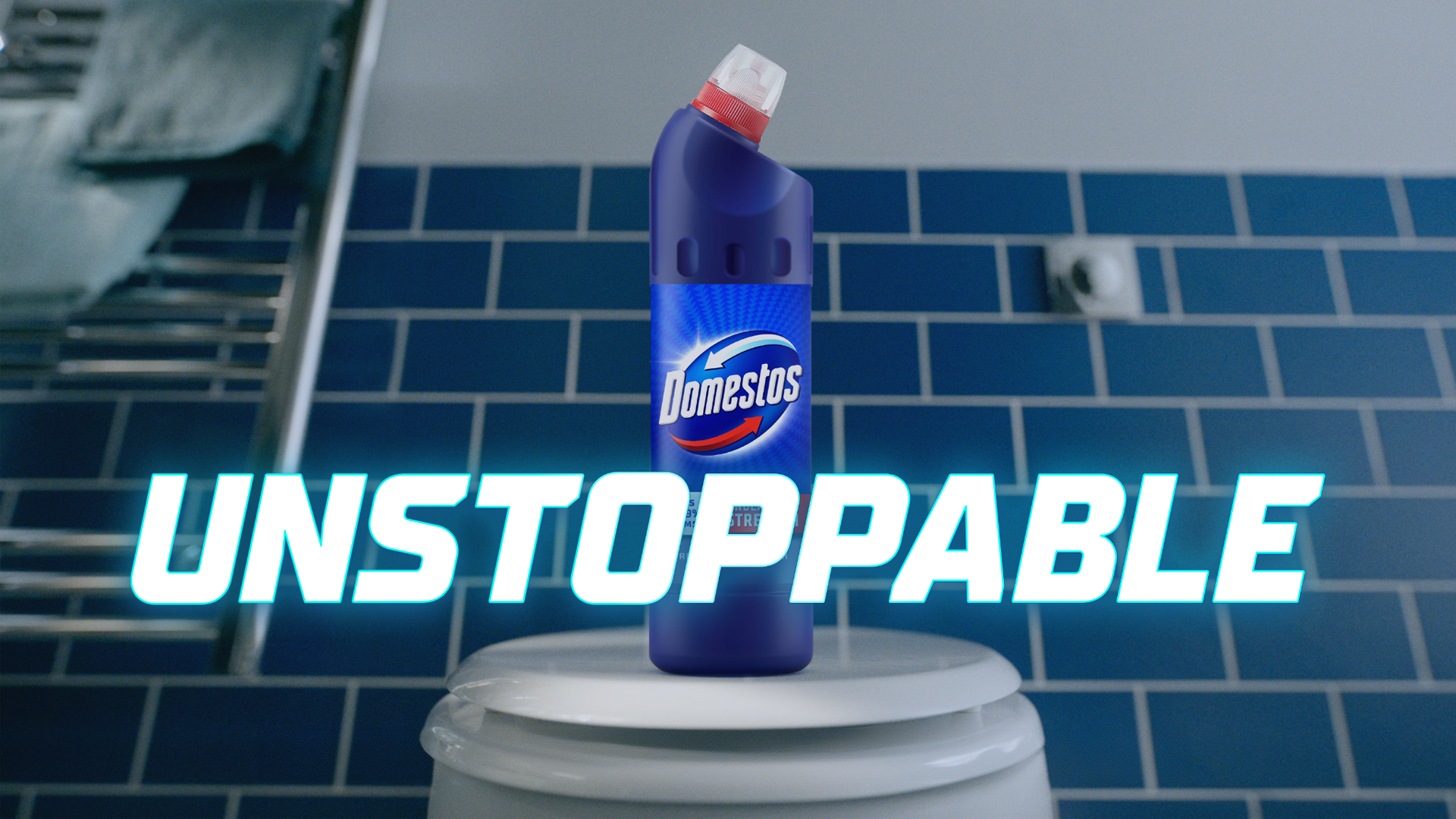 A bottle of Domestos on top of a toilet with the word “Unstoppable” overlaid. The toilet is in a bathroom with blue tiles and white walls. Two towels hang on a radiator to the left of the toilet.