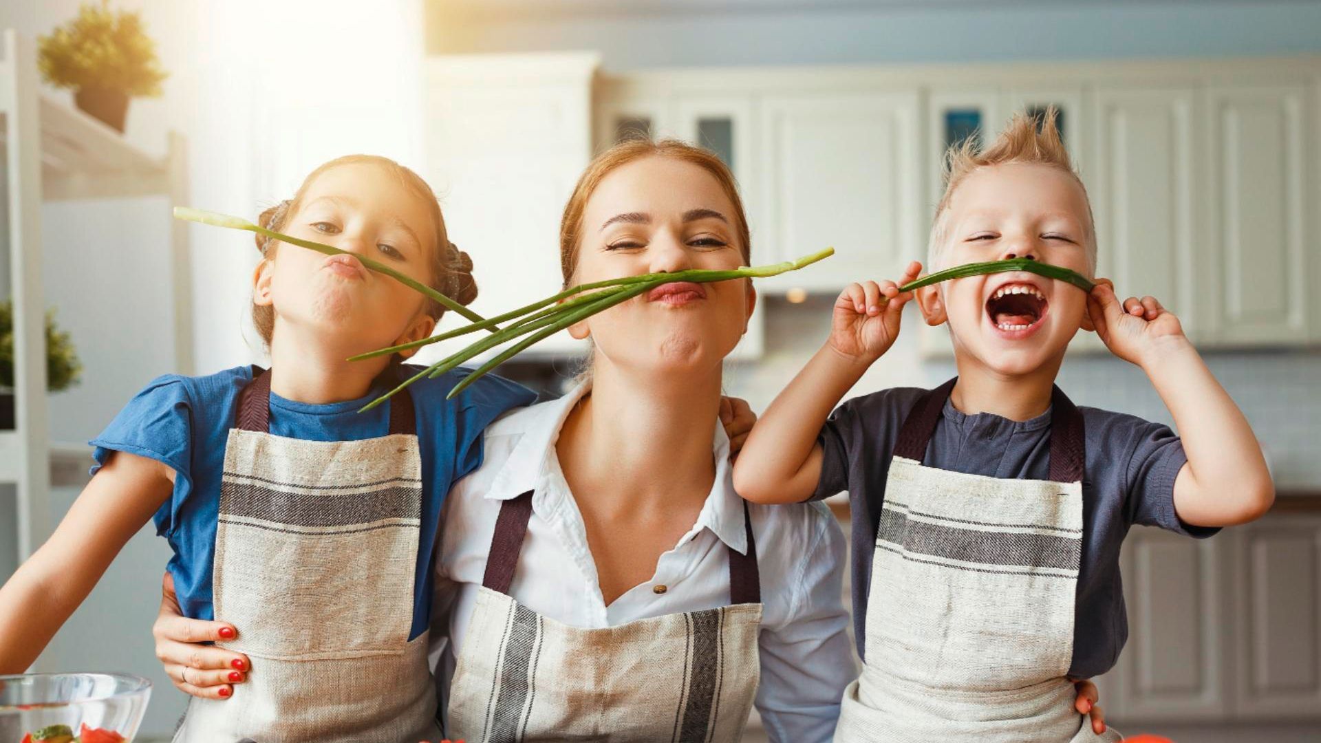 girl, woman and a boy with a scallion above their lips in the kitchen