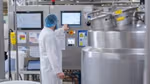 Ice cream factory worker in a white lab coat and hairnet attending a machine that’s part of the manufacturing process