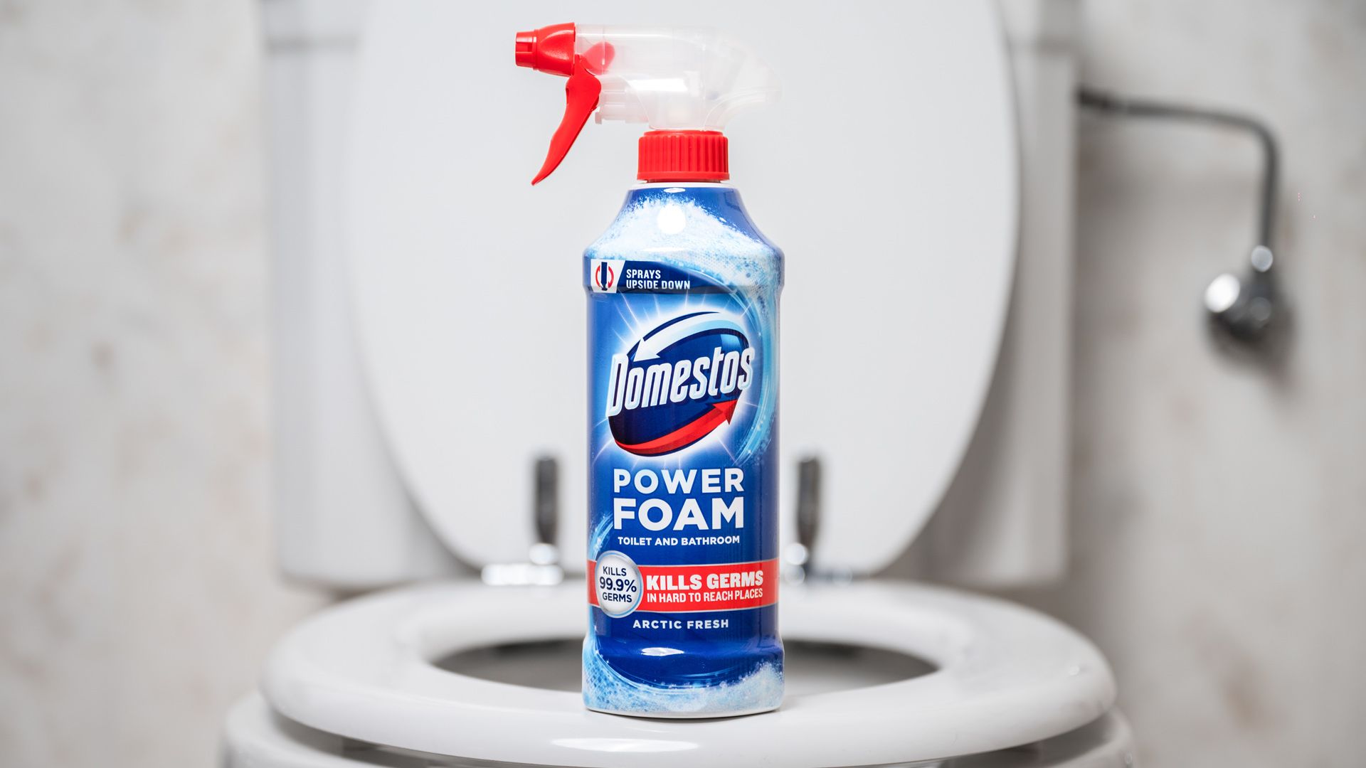 The new Domestos Power Foam Spray bottle sits on the edge of a bath. The bath and shower in the background are blurred