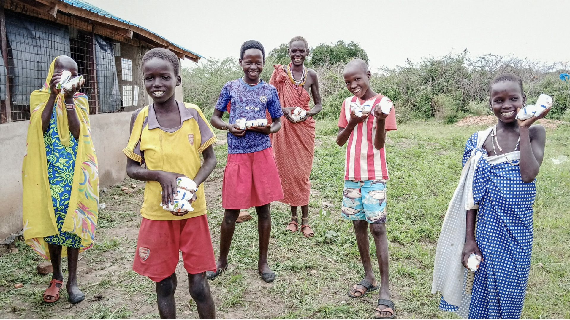 Six smiling children in rural South Sudan showing off the Unilever soap bars they have been given to wash their hands