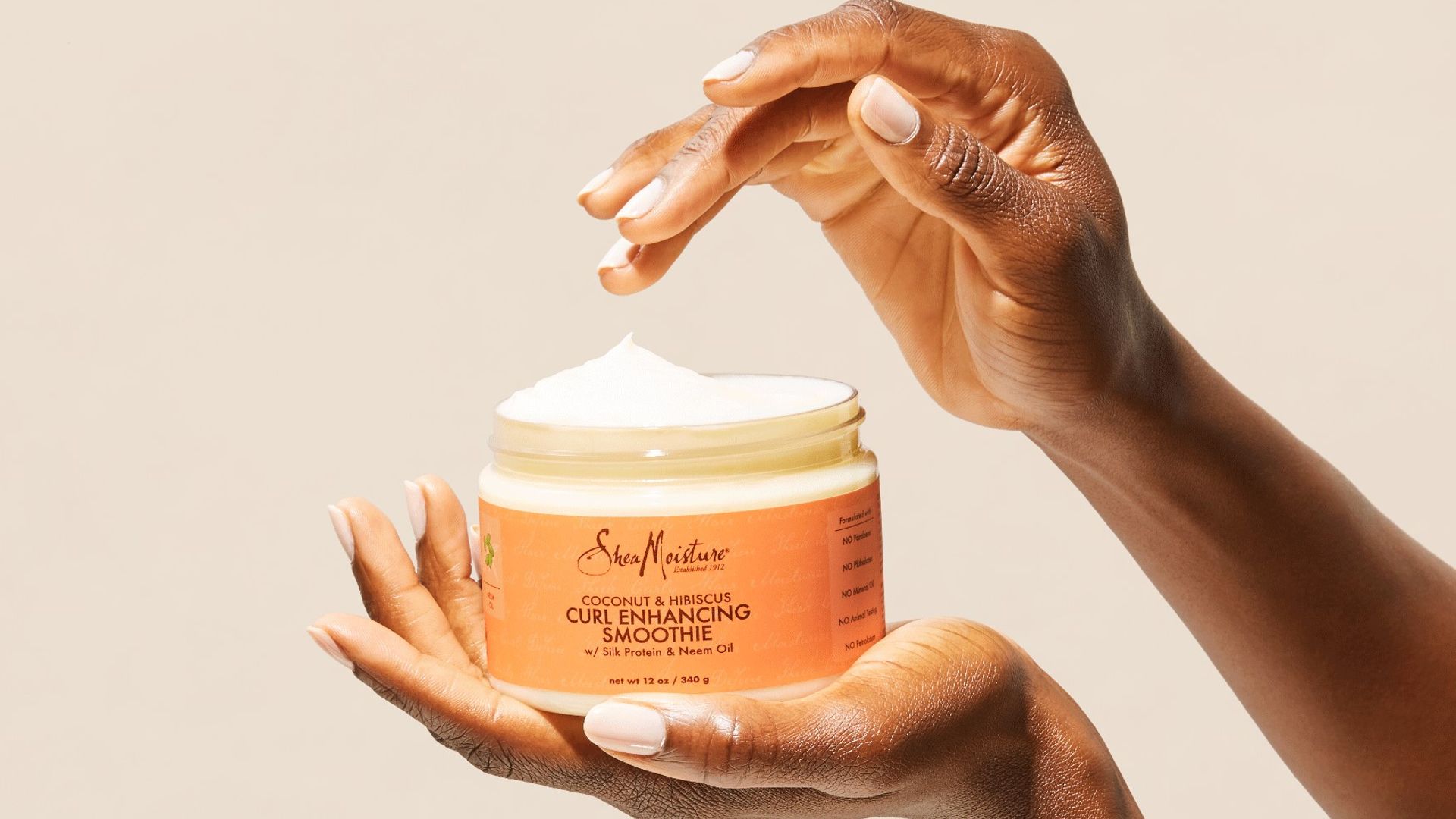 Close up of a Black woman’s hands as she dips fingers into a jar of Shea Moisture Curl Enhancing Smoothie hair product