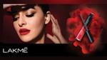 A woman with bold red lips and smokey eye make-up gazes away from the camera, holding a tube of Lakmé lip mousse.