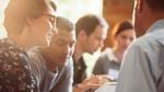 A group of people in a huddle looking at a tablet