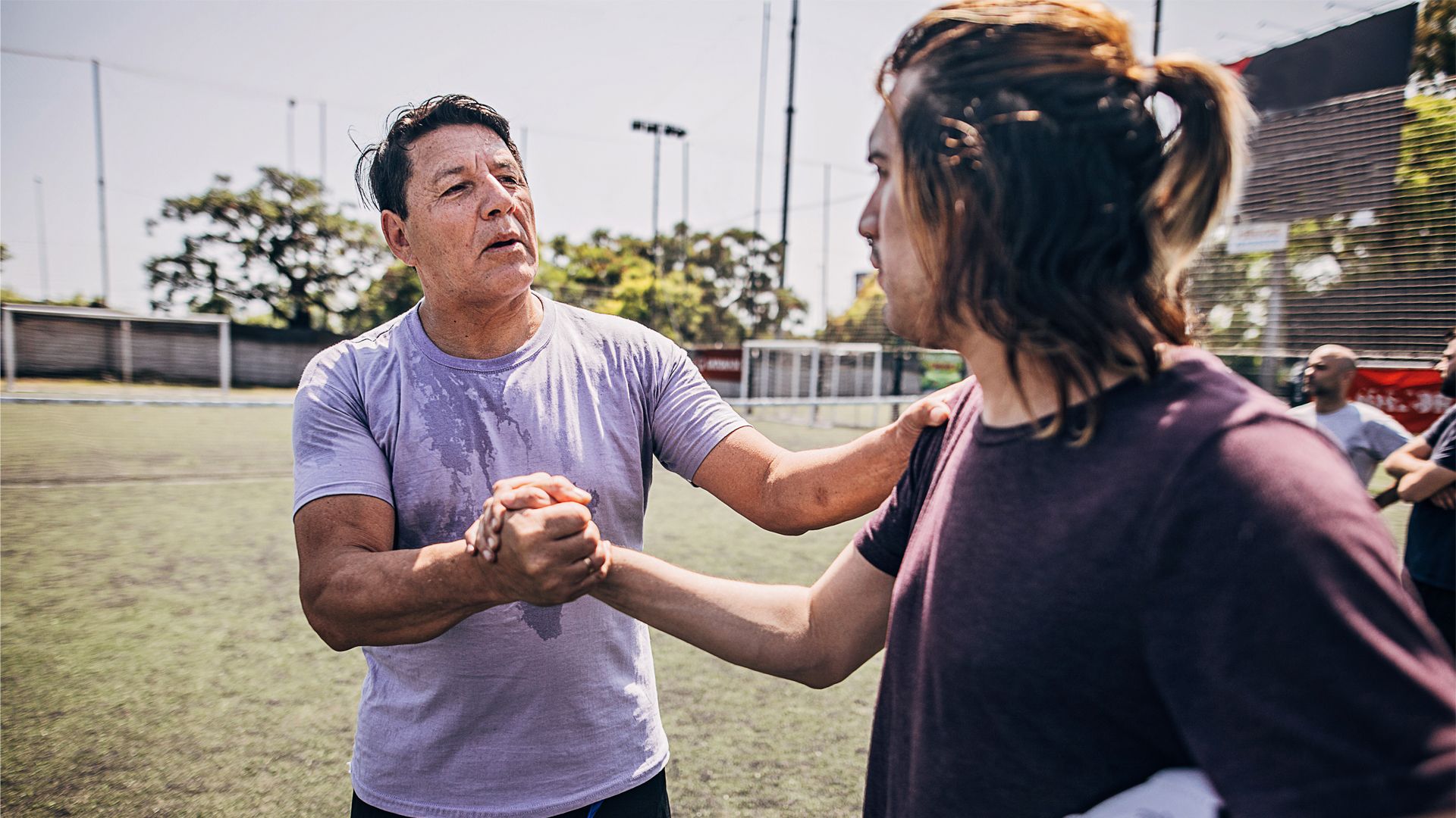 Two people on a sports field grasping their right hands.