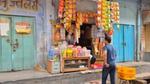 A man shops at a small store in rural India. Colourful goods are displayed on a table and hanging from the wall.