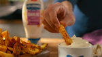 Close-up of a chip being tipped into a bowl of Hellmann’s flavoured garlic mayo.
