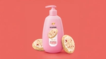 A pink bottle of Strawberry Crumb Cake hand wash from the Dove Crumbl collaboration. Crumbl cookies either side. Coral pink background.