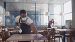 Two people wearing facemasks wiping down tables in a restaurant