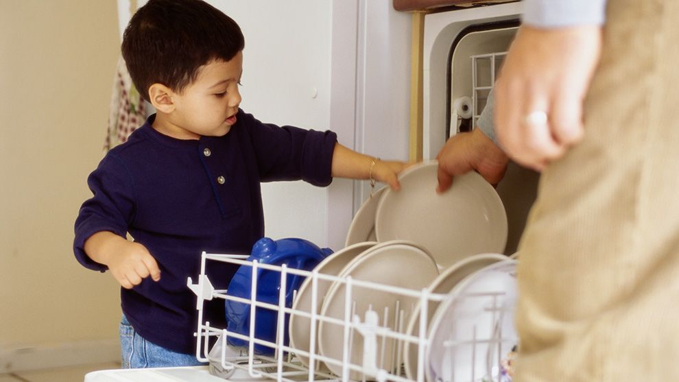 Young child helping to load dishes into a dishwasher