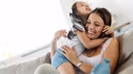 A woman laughing on a couch while a young girl hugs her tightly