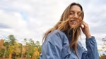 A girls sat outdoors wearing a blue windbreaker. The wind blows through her hair.