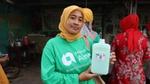 A women in a hijab and green shirt holding a bottle of product.